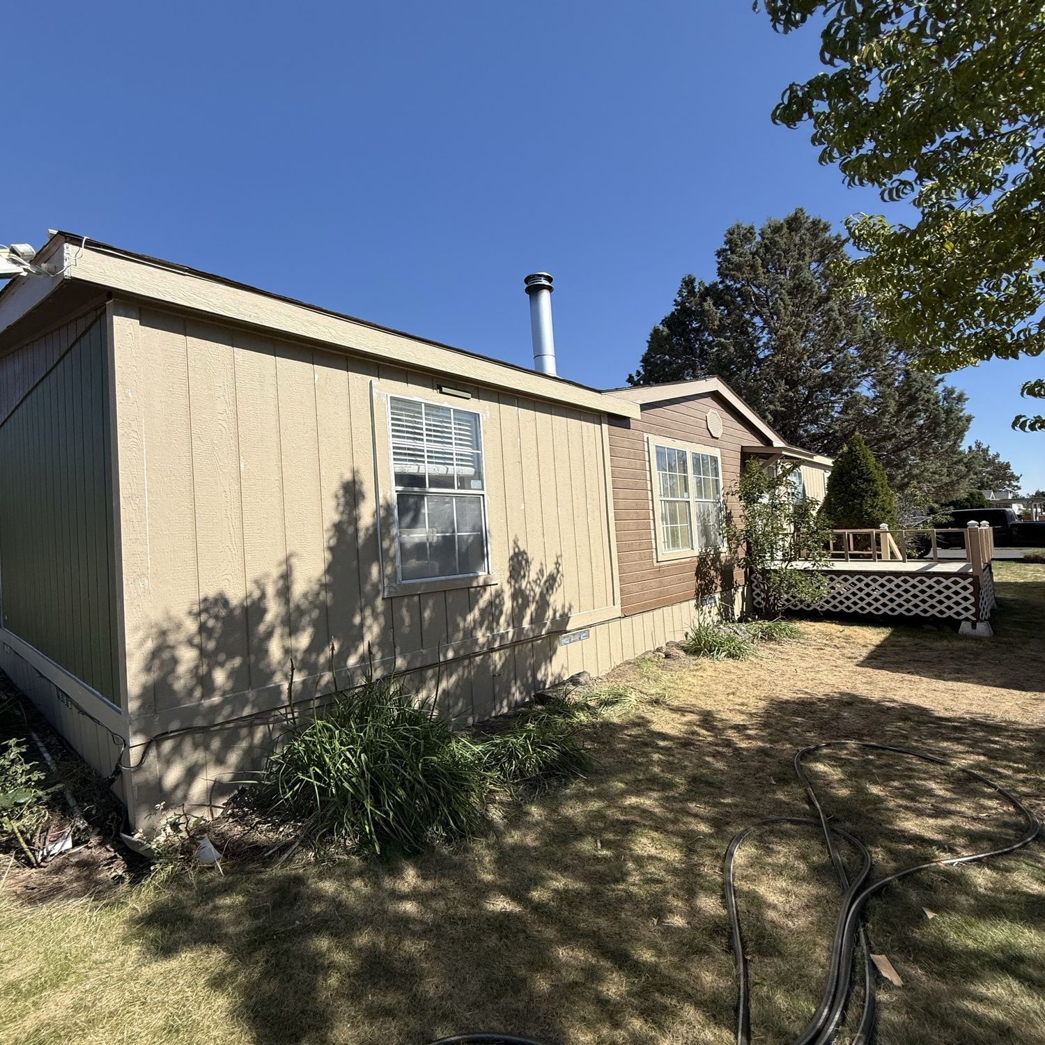 Beige house exterior with windows, chimney, and a small fenced porch under a clear blue sky.