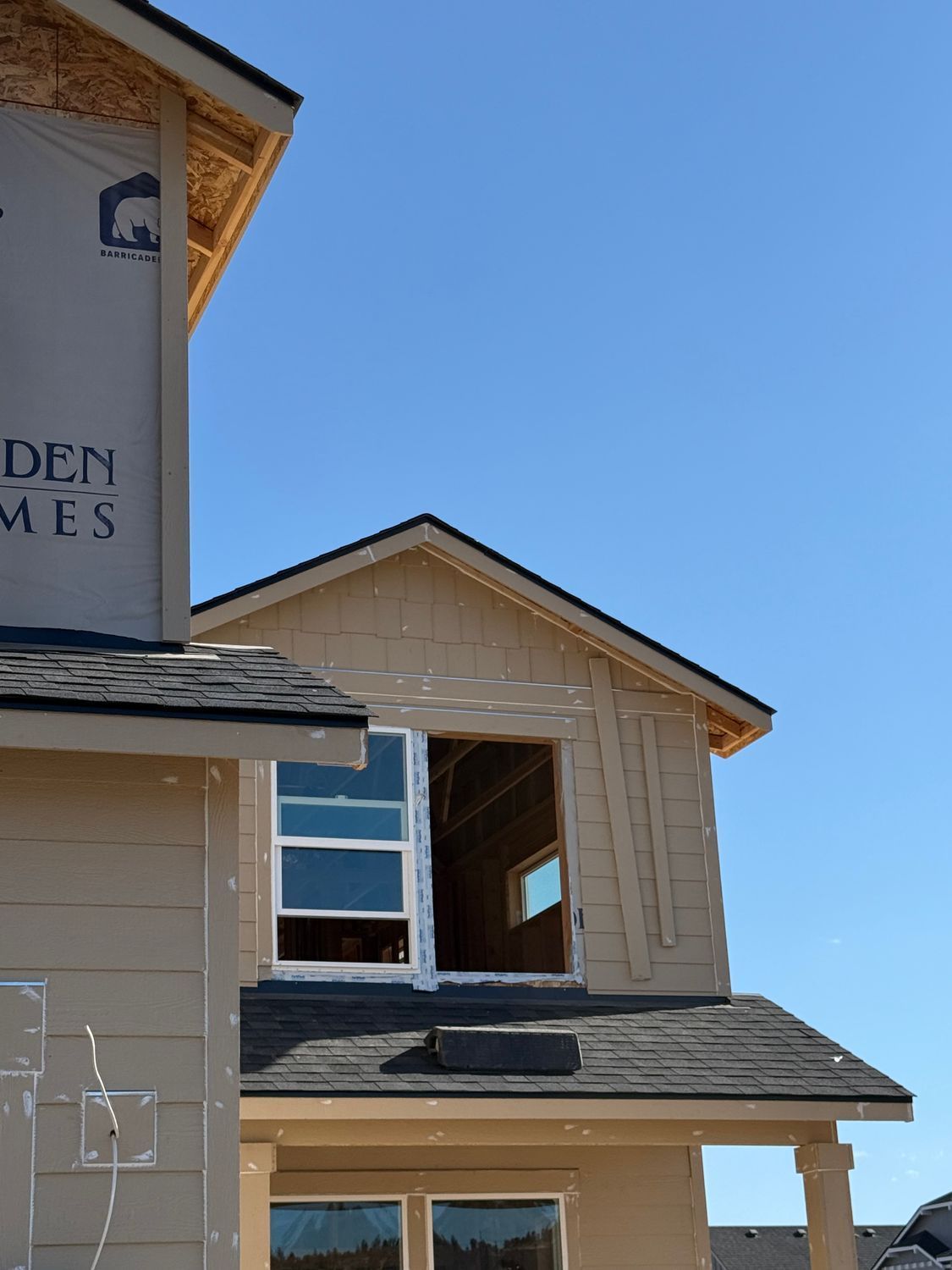 Tan house with dormer windows and dark shingled roof against a clear blue sky
