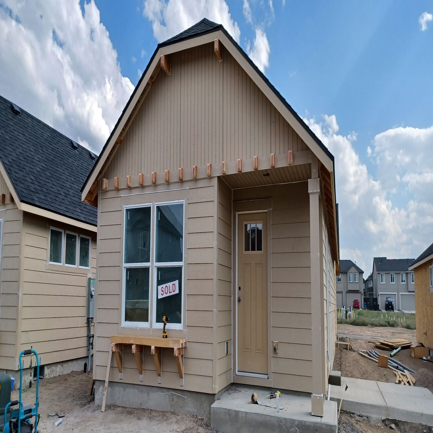 Small tan house under construction with unfinished porch and windows on a new residential lot