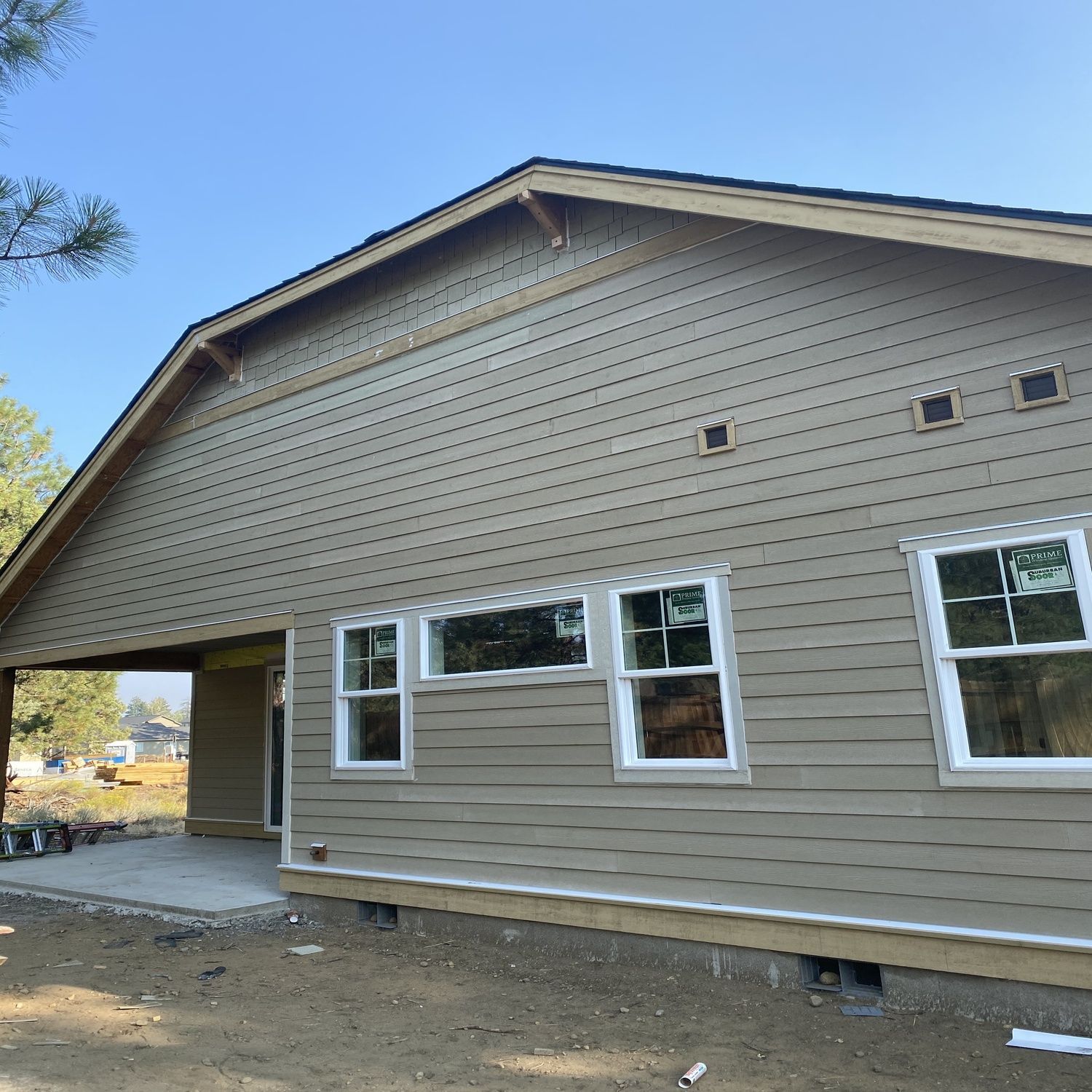 Exterior of a tan house with white-trimmed windows and a covered side porch under construction