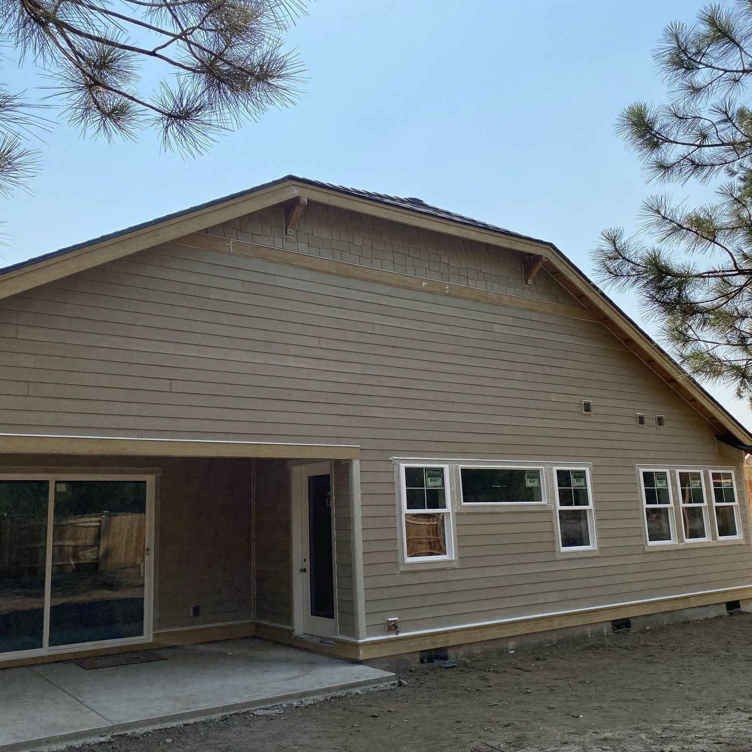 Tan house with covered patio and white-trimmed windows, viewed from the front yard.