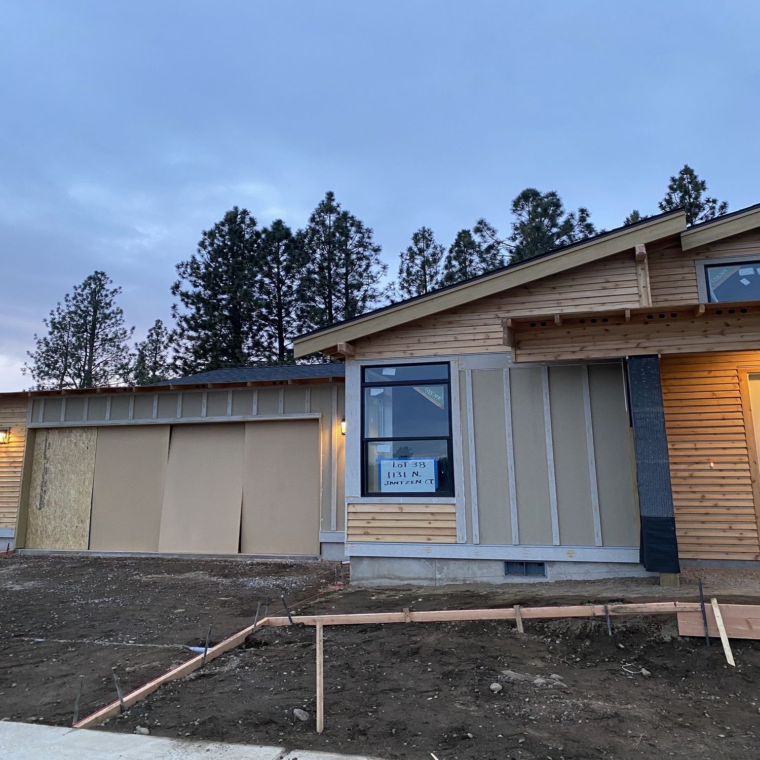 Partially finished house exterior with wood siding, windows, and bare dirt yard at dusk