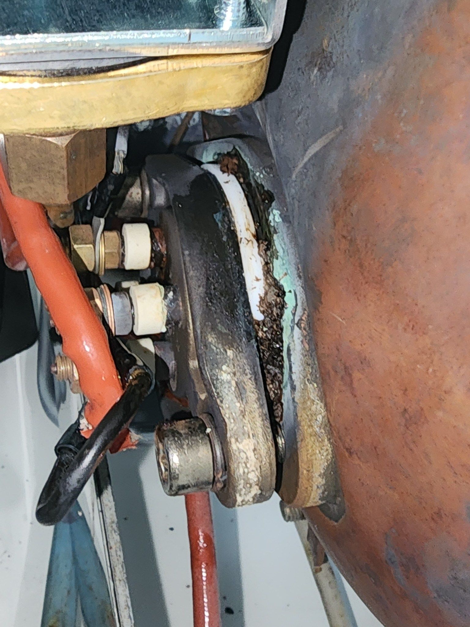 Close-up of a corroded metal pipe joint with bolts, orange tubing, and rusted hardware on a wall