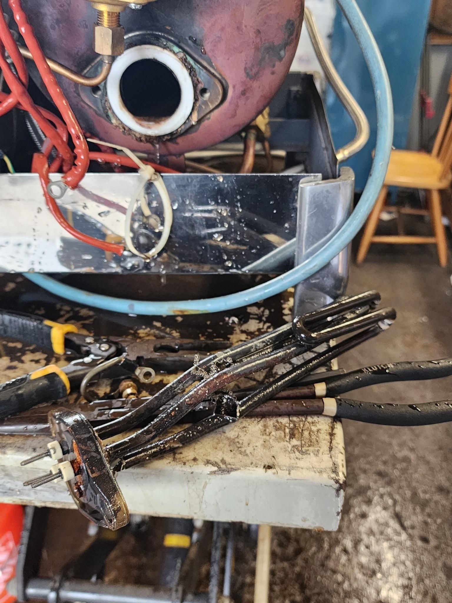Close-up of a greasy engine part and metal tools on a dirty workbench with a transparent container.