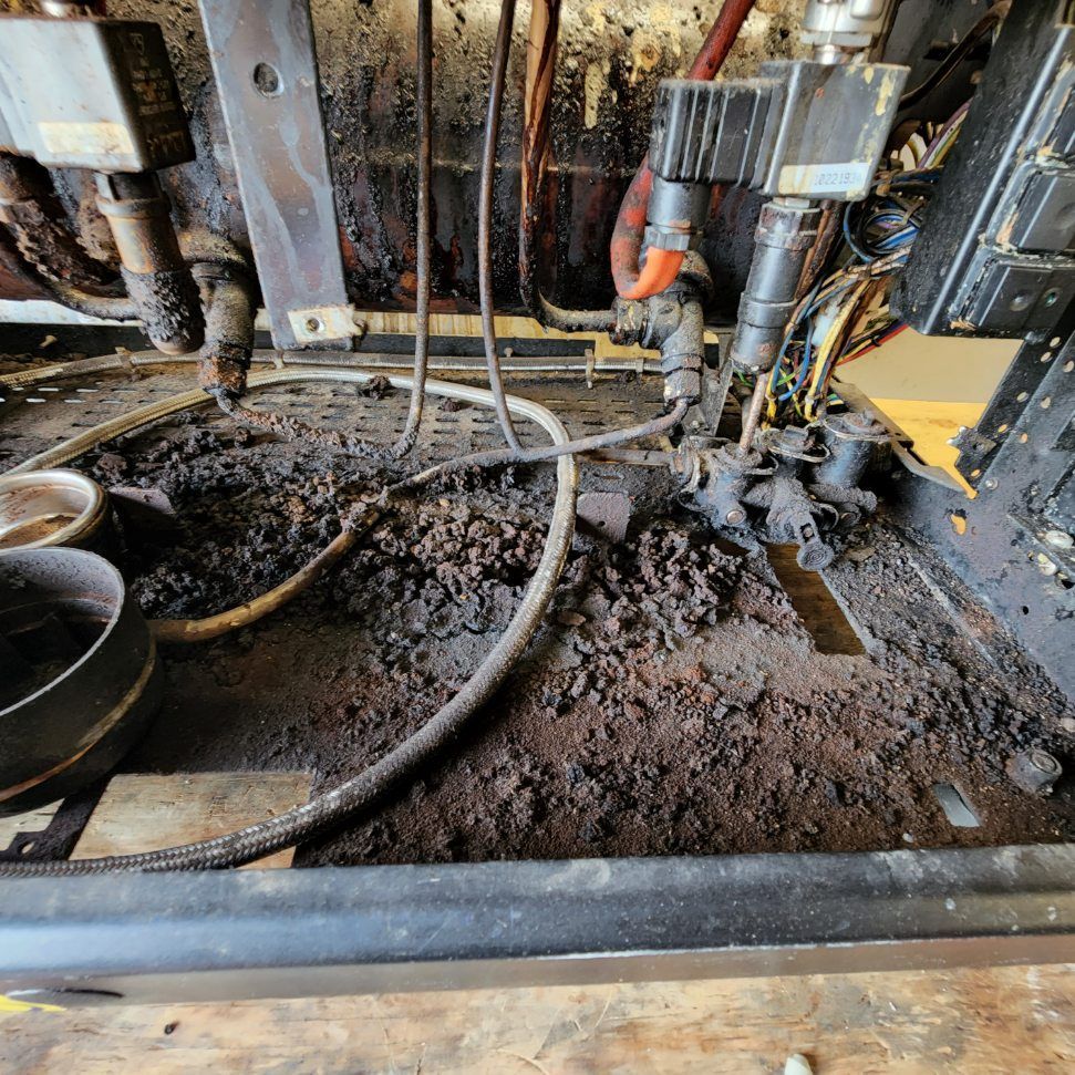 Mud-covered industrial machinery and hoses inside a dirty metal compartment