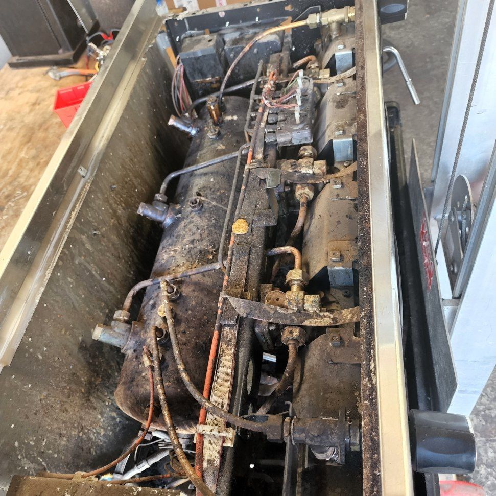 Dirty industrial machine with exposed pipes, wiring, and metal components inside a large enclosure