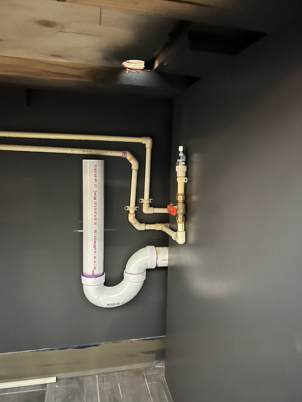 Plumbing pipes and a valve inside a dark gray utility cabinet with a small ceiling light.
