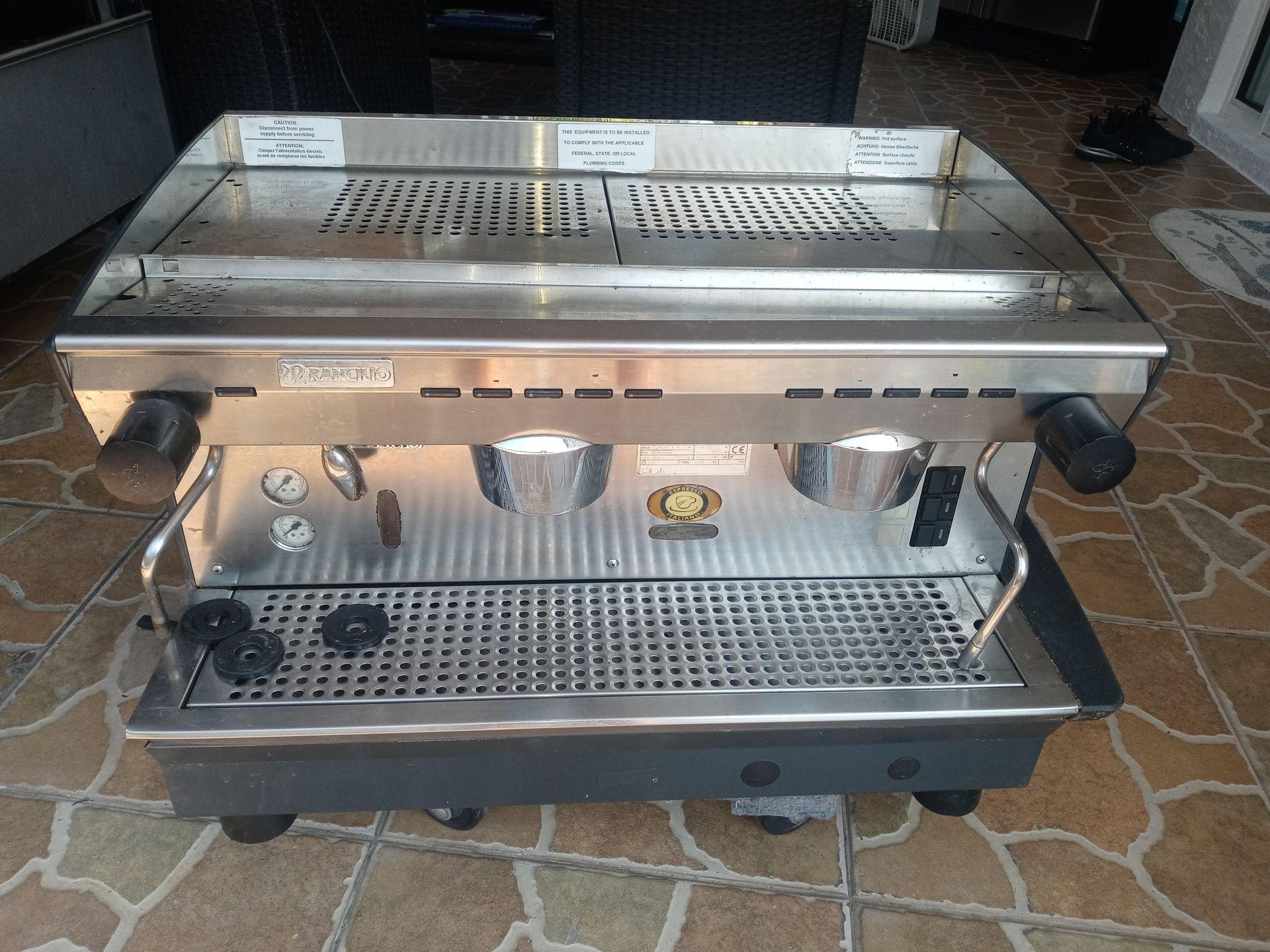 Stainless steel espresso machine with dual group heads on a tiled floor.