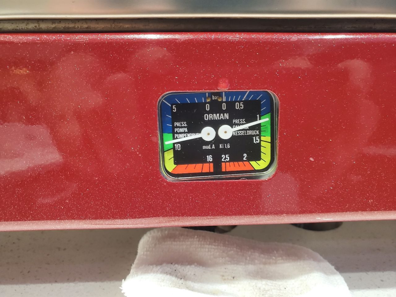 Close-up of a small multicolor gauge mounted on a red metal surface.