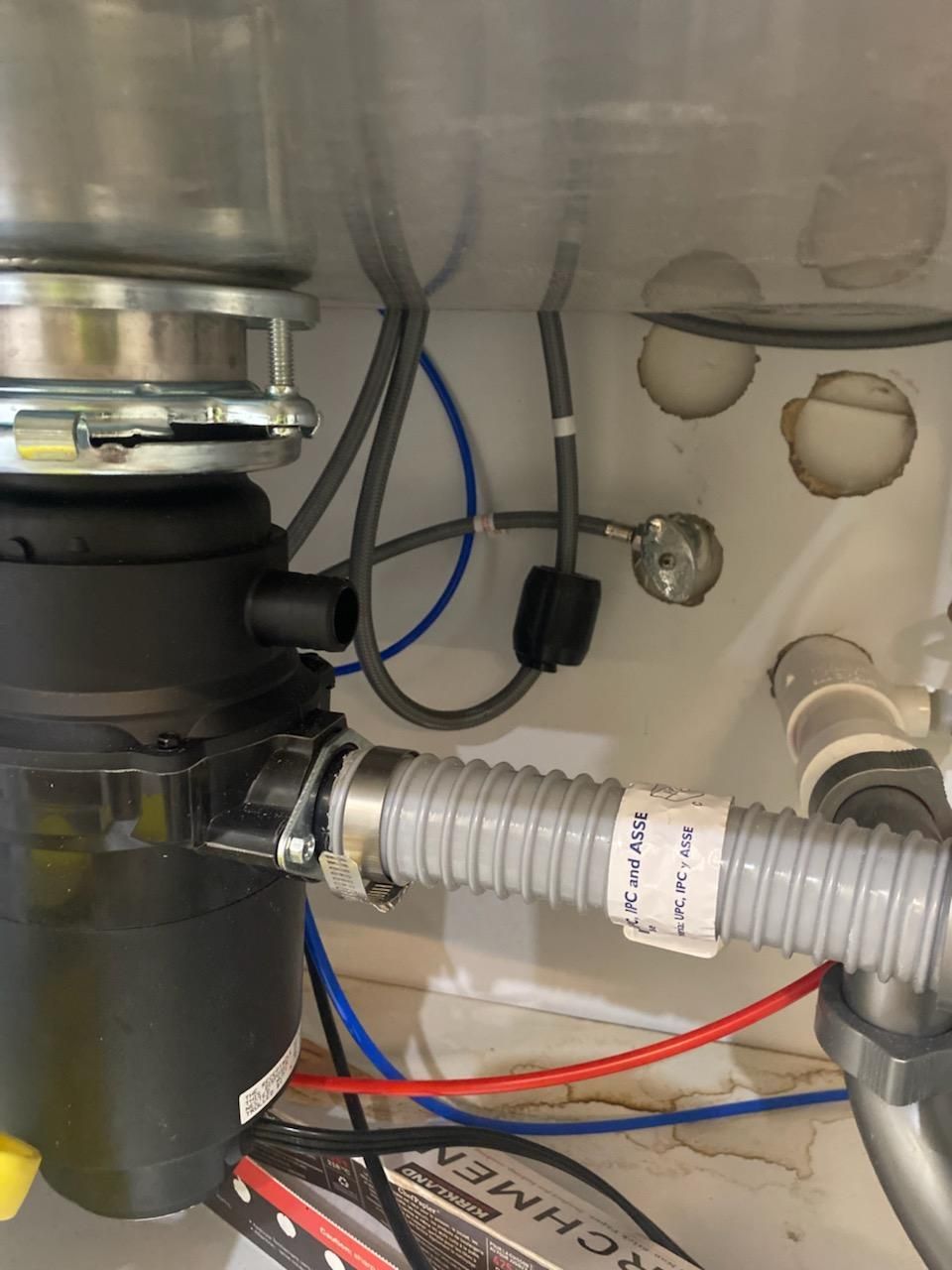 Under-sink garbage disposal with gray hose and exposed wires in a cabinet