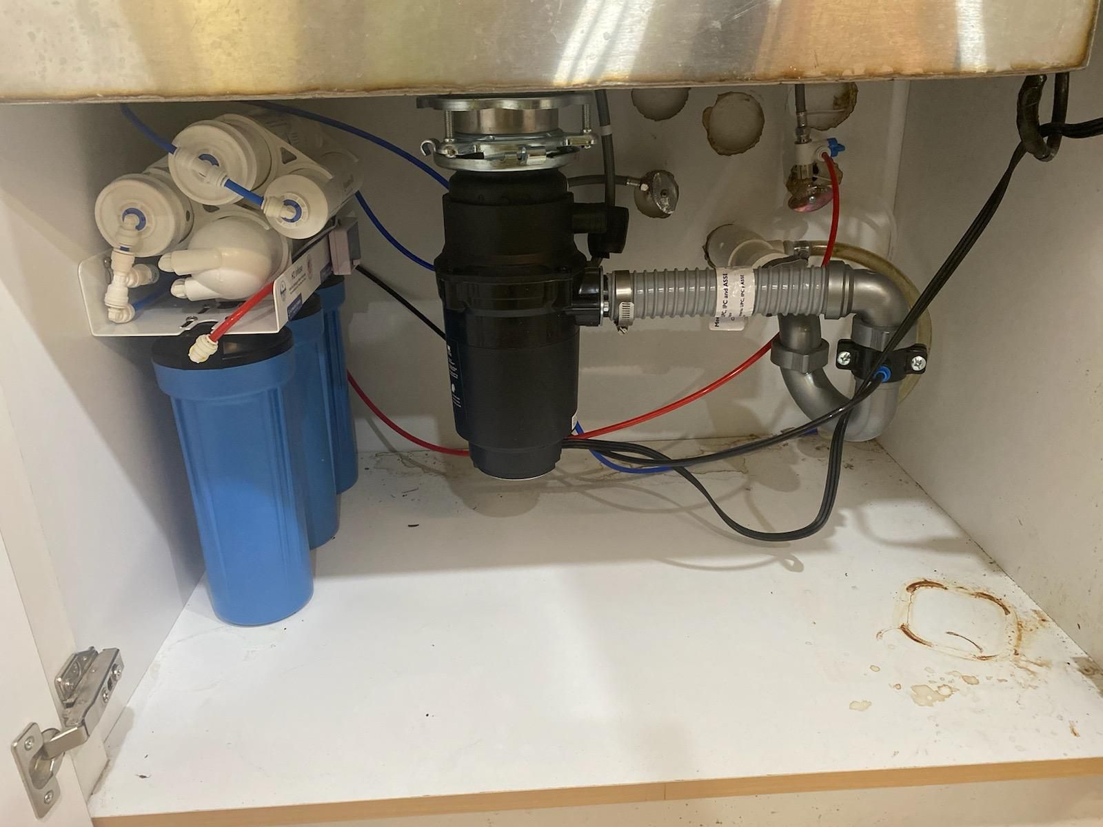 Under-sink plumbing with pipes, filters, and valves in a white cabinet under a countertop