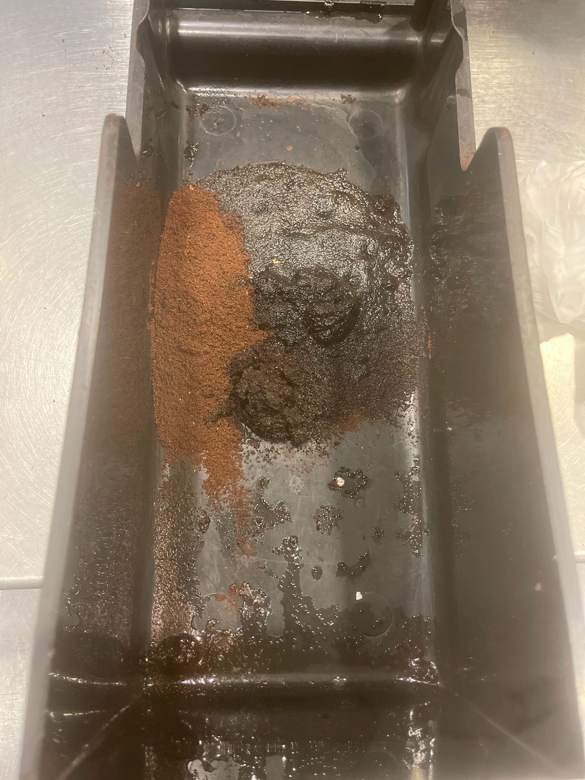 Close-up of a black tray with scattered brown granules and a dark mound in the center.