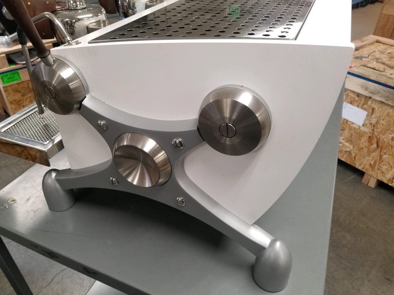Close-up of a stainless steel industrial machine with knobs, mounted on a white housing and gray base