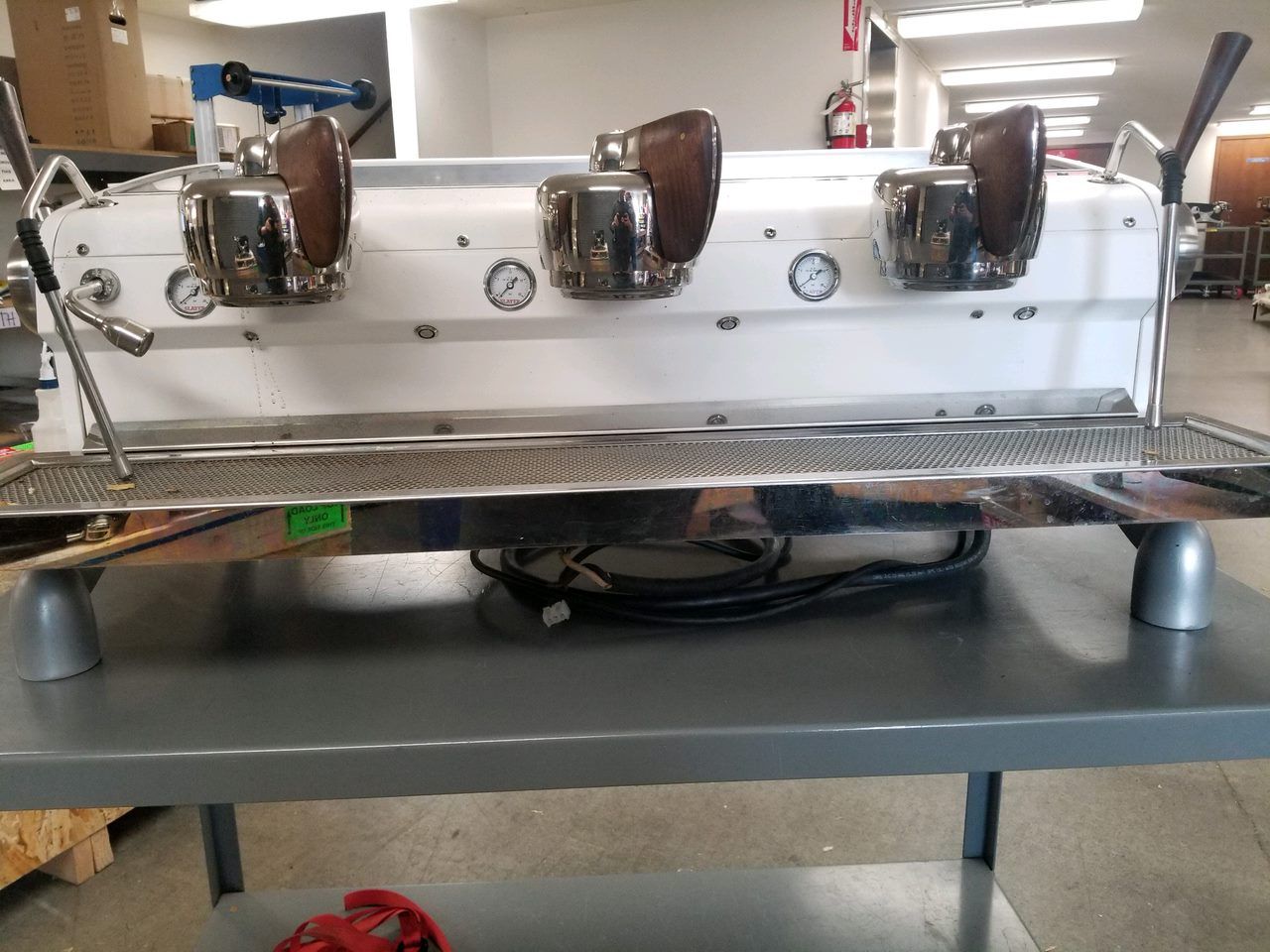 Industrial espresso machine with three brown group heads on a metal counter in a workshop setting