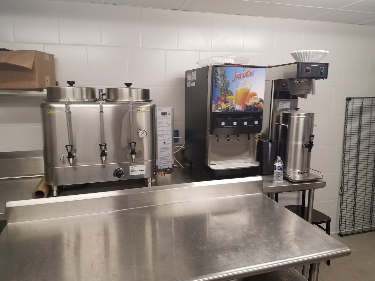 Stainless steel beverage dispensers and a soda machine on a counter in a kitchen or break room