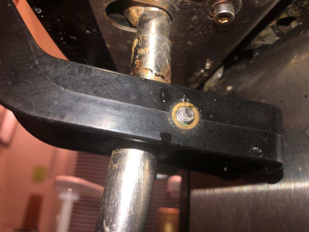 Close-up of a black clamp with a rusted bolt on a metal pole beneath a machine.