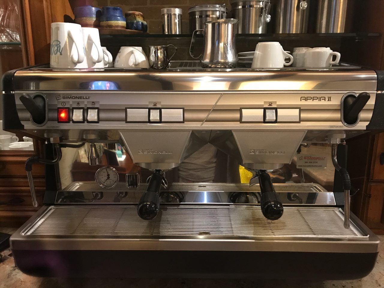 Stainless steel espresso machine with cups on top in a café setting
