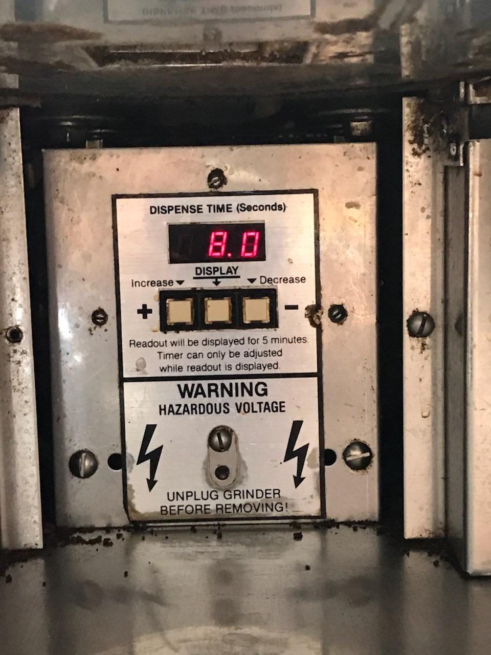 Close-up of a metal control panel with a red digital display and high-voltage warning signs.