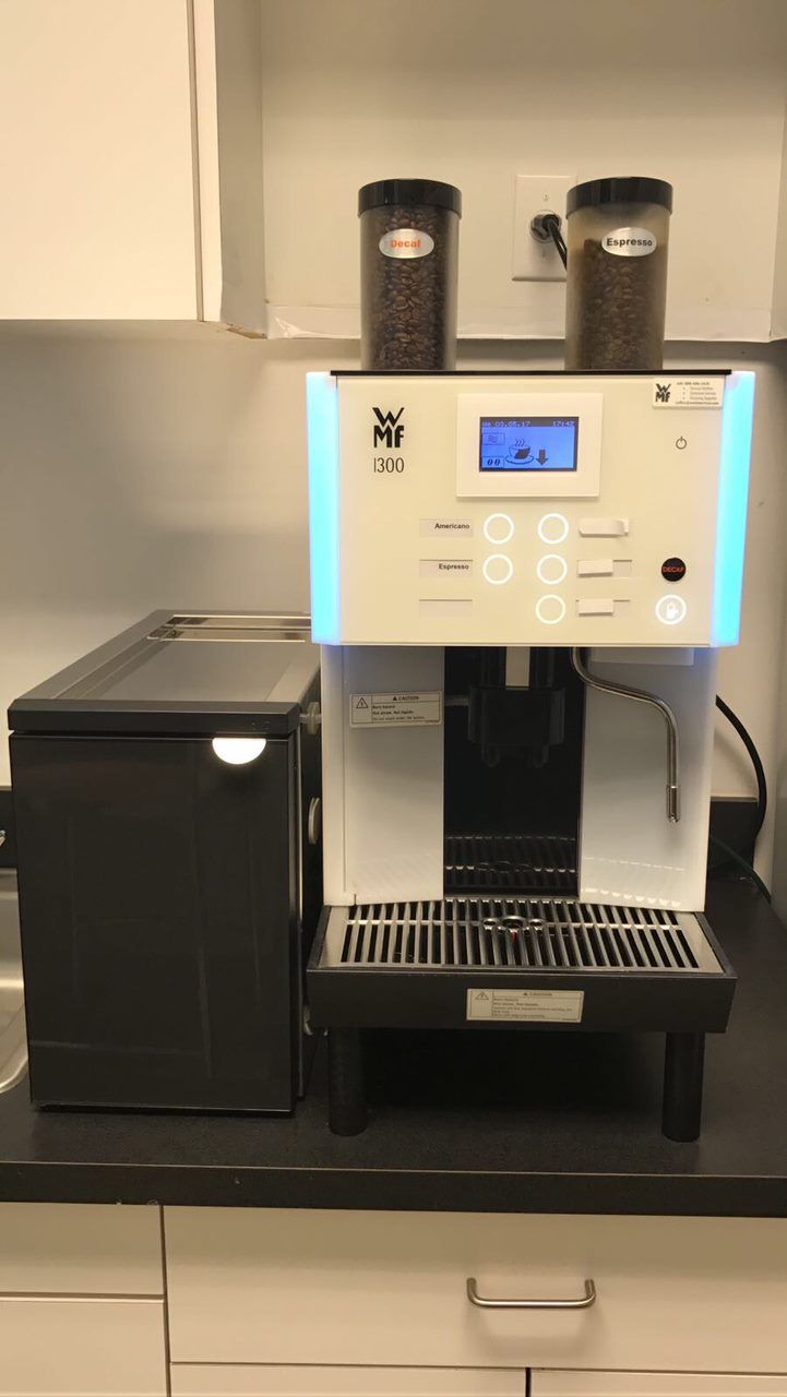 Silver espresso machine with blue display beside a black mini fridge on a countertop