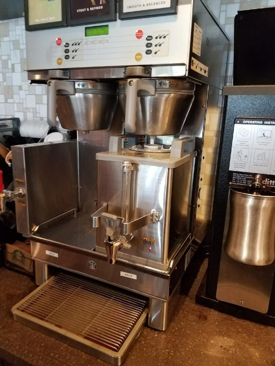 Stainless steel dual coffee machine with bean hoppers and drip tray in a café area