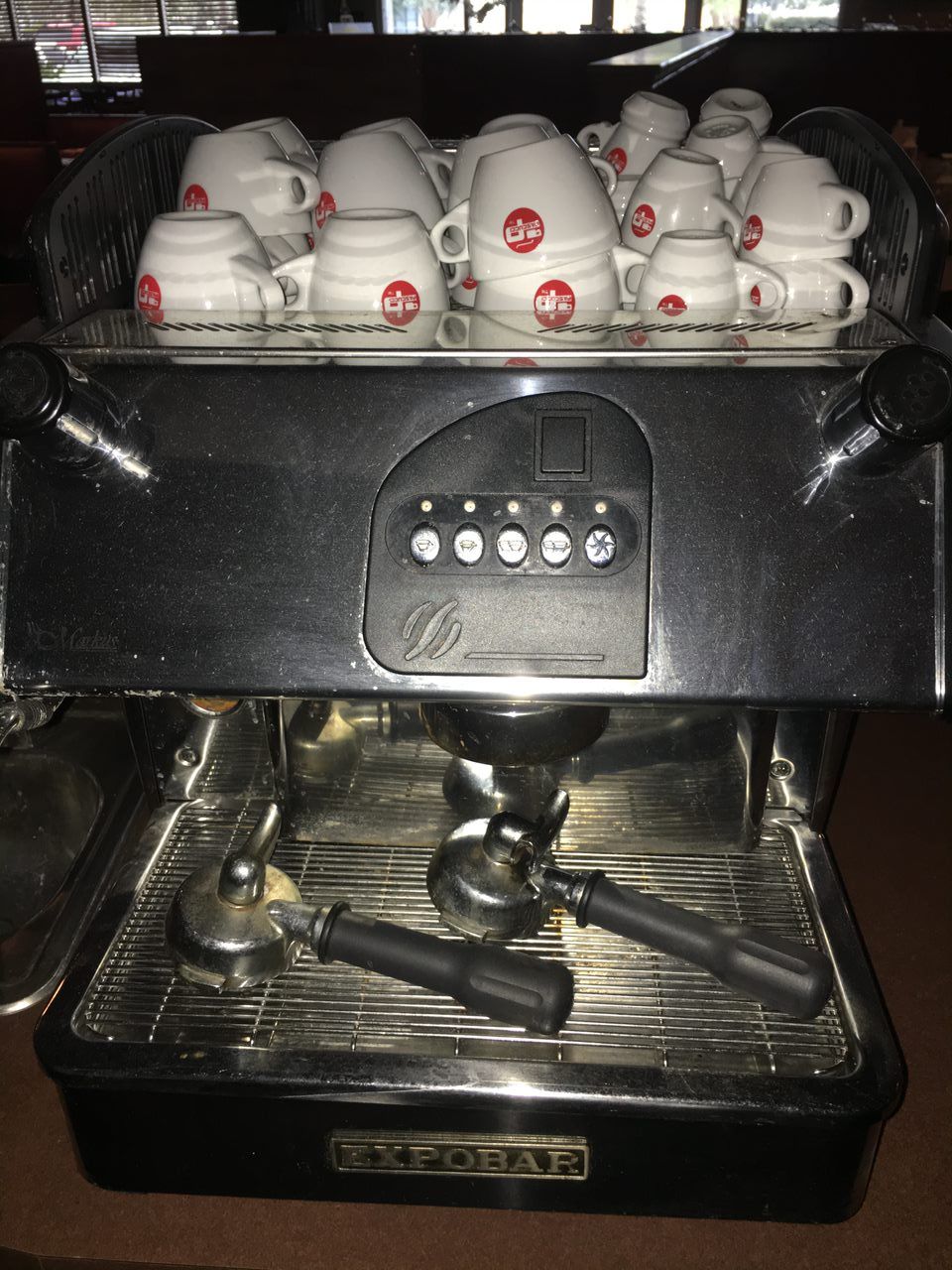 Espresso machine with a row of white cups on top and portafilter handles below