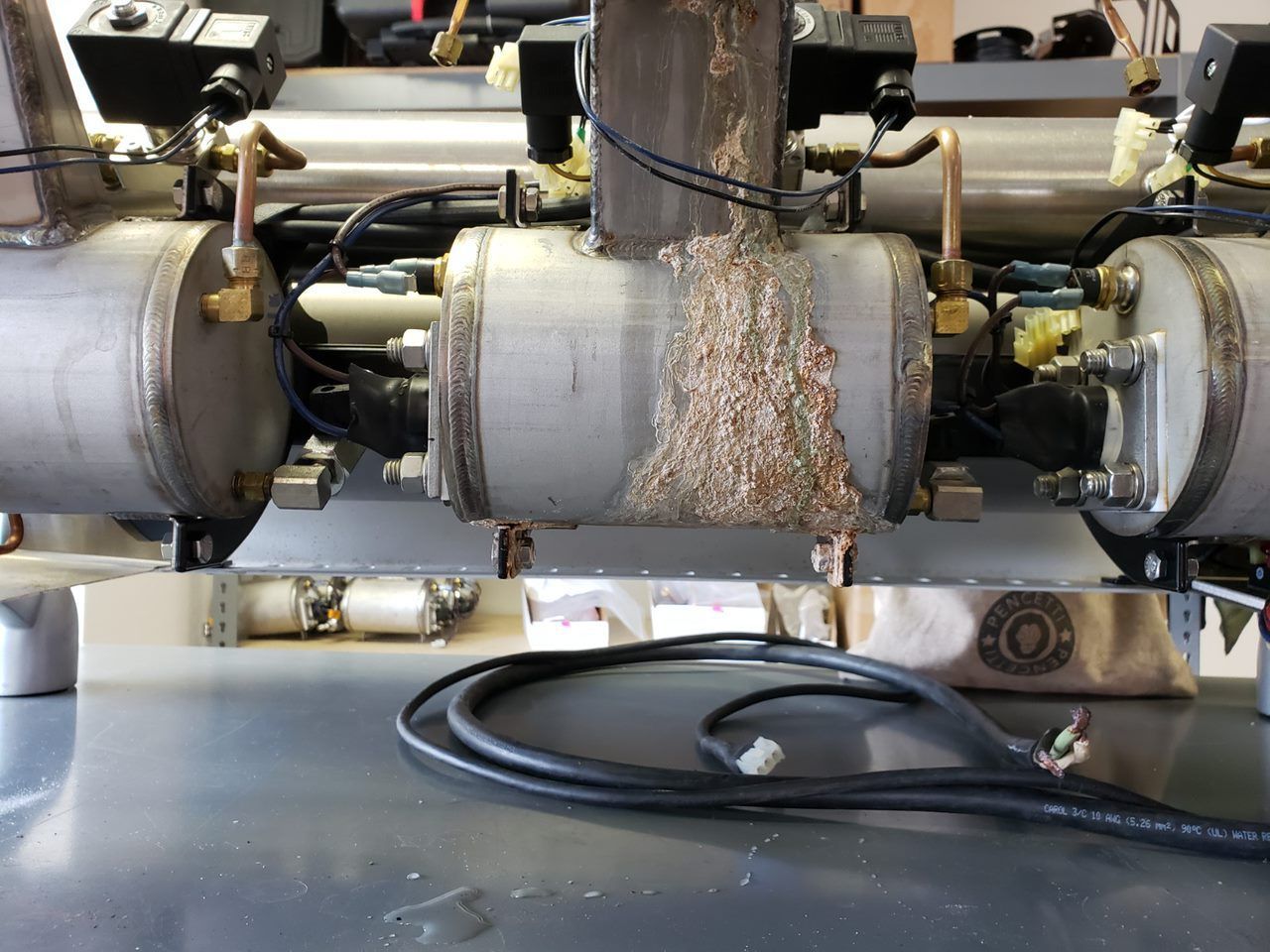 Industrial machine with rotating drums and debris buildup on a metal workbench.