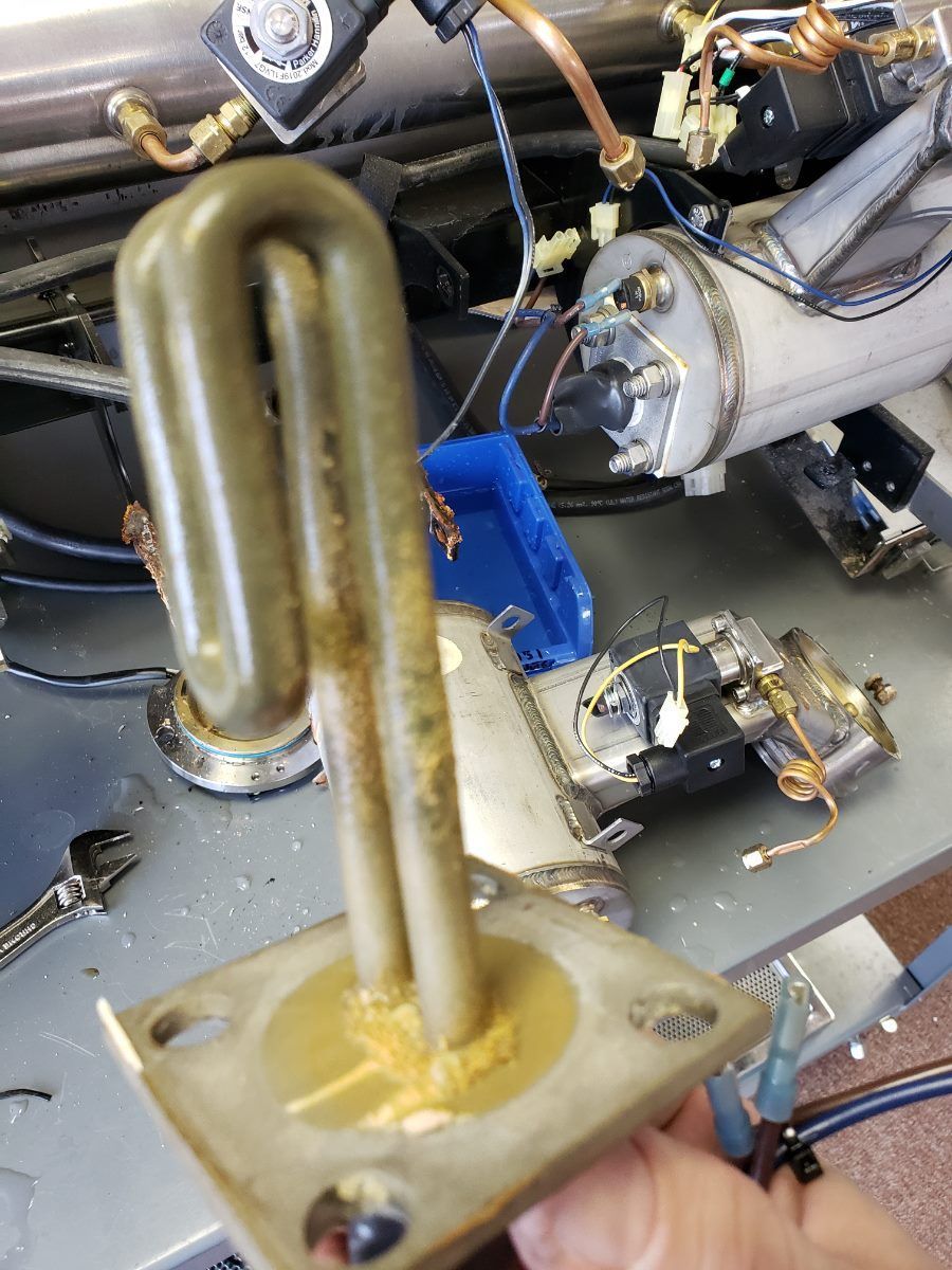 Close-up of brass U-shaped metal tubing and fittings on a gray mechanical surface, with wires and engine parts nearby