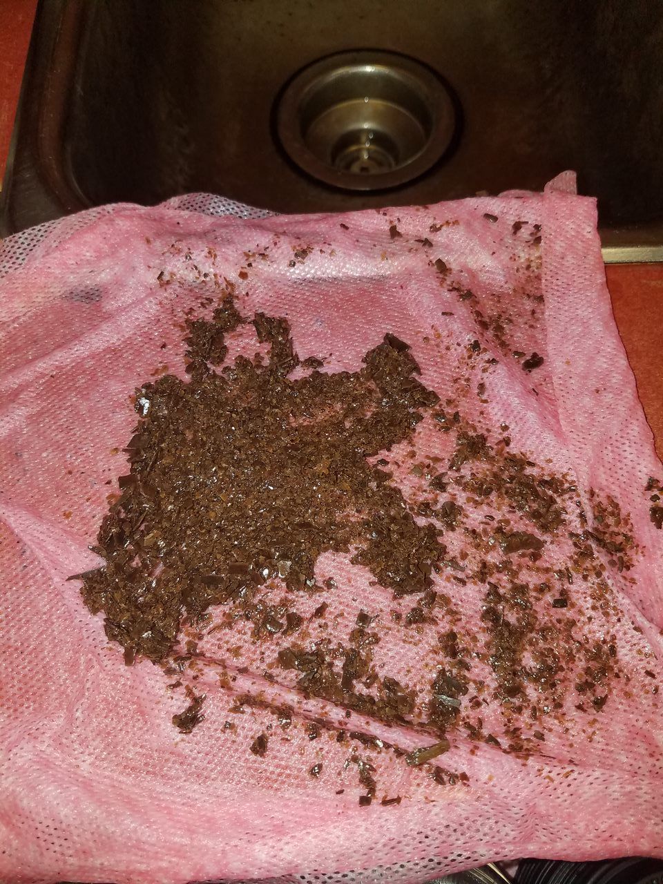 Brown debris on a pink cloth laid over a kitchen sink drain