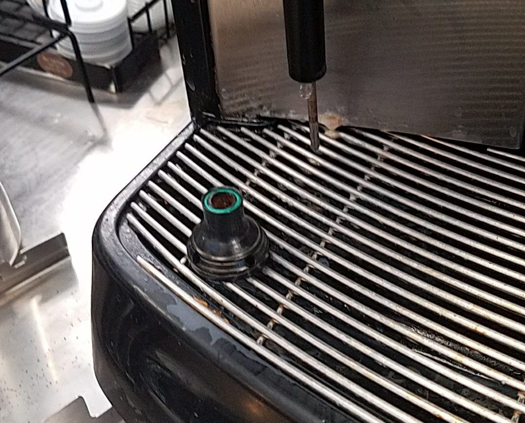Black coffee machine drip tray with a cup and metal grate in a kitchen or café setting