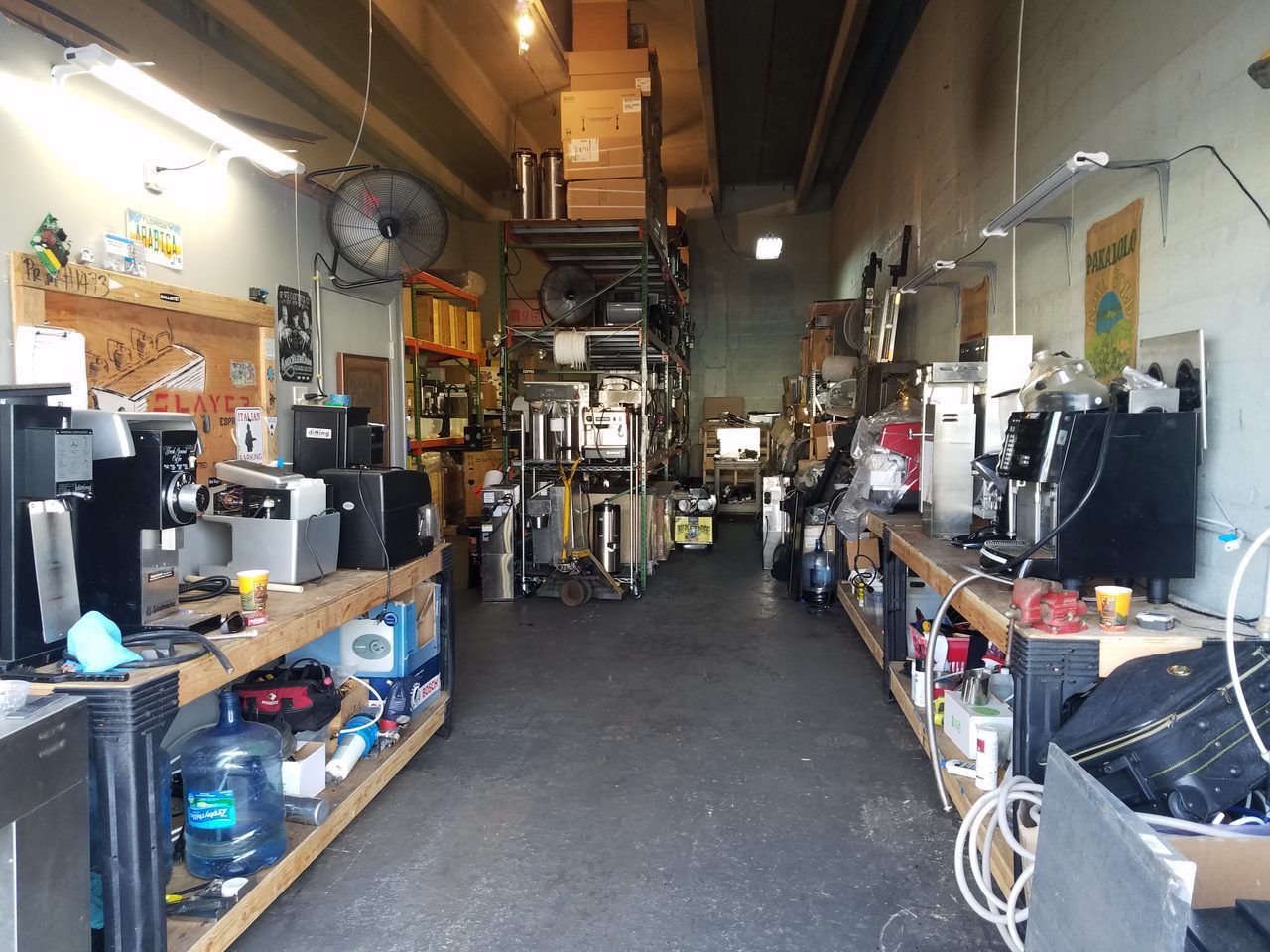 Narrow workshop aisle lined with shelves of electronics and equipment under warm overhead lights.