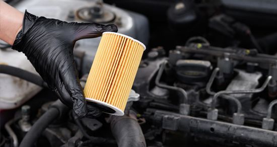 Gloved hand holding a yellow engine oil filter in a car engine bay