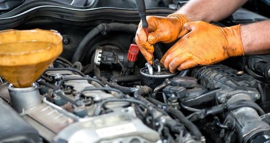 Mechanic with orange gloves working under a car hood, using a tool on the engine