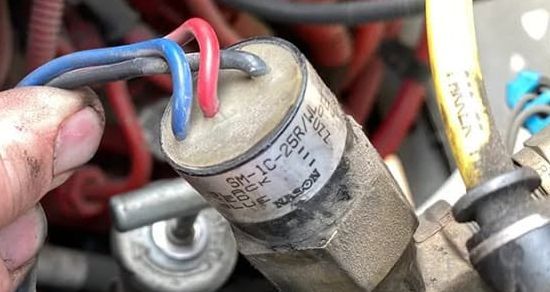 Close-up of a cylindrical electrical component with red and blue wires attached in a cluttered machine bay