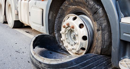 Flat truck tire with a detached wheel rim on the roadside, close-up of a damaged semi-truck wheel
