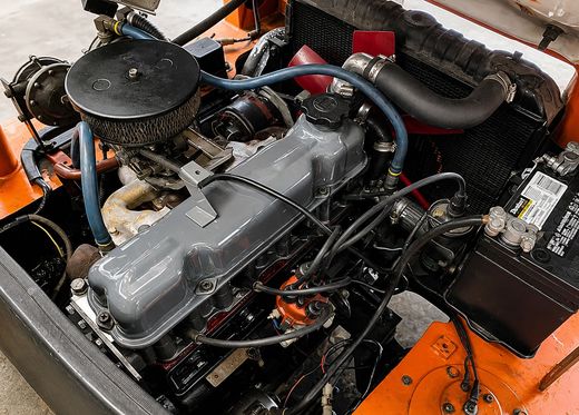 Close-up of a classic car engine bay with orange body panels and black hoses and components