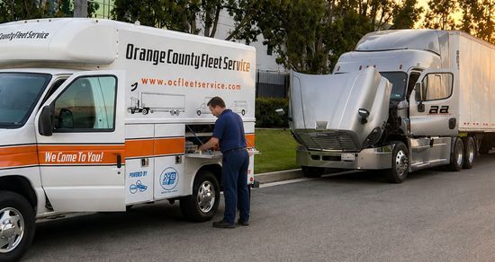 White service vans parked roadside, one being loaded by a worker; Orange County Emergency Services vehicle in front.