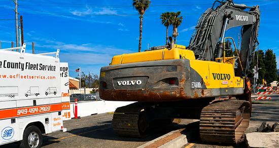 Yellow Volvo excavator on a trailer at a construction site under a blue sky