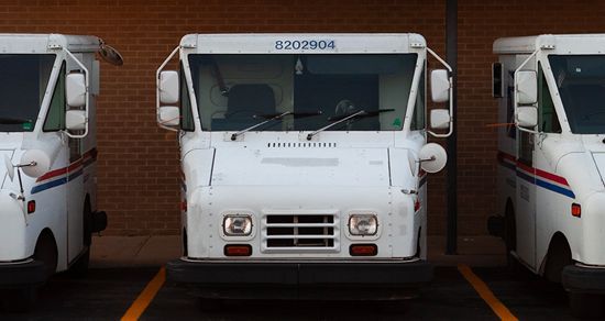 White delivery truck parked between two trucks in a warehouse loading bay