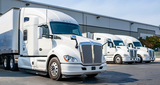 White semi-trucks parked outside a warehouse on a sunny day