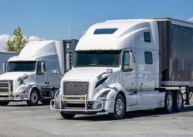 Two white semi-trucks parked in a lot under a clear sky