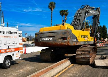 Yellow Volvo excavator on a flatbed truck beside a road under a blue sky