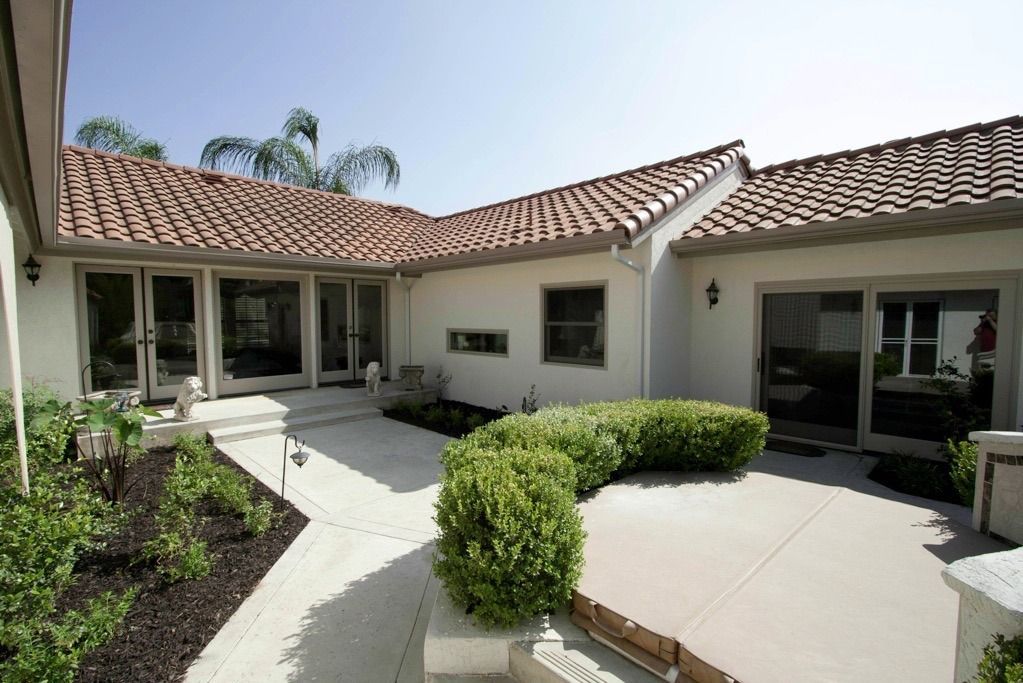 Courtyard of a Mediterranean-style home with tiled roof, white walls, and a curved concrete walkway
