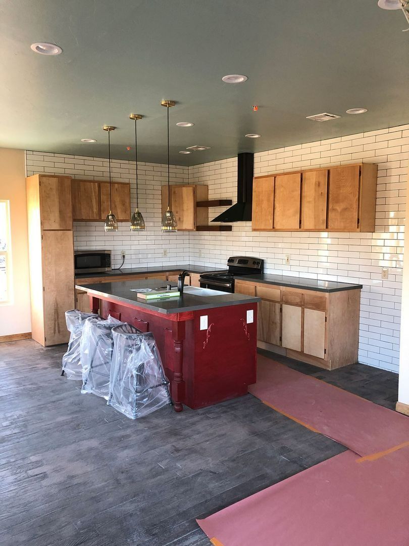 Unfinished kitchen with wood cabinets, gray floor, and a red island wrapped in plastic.