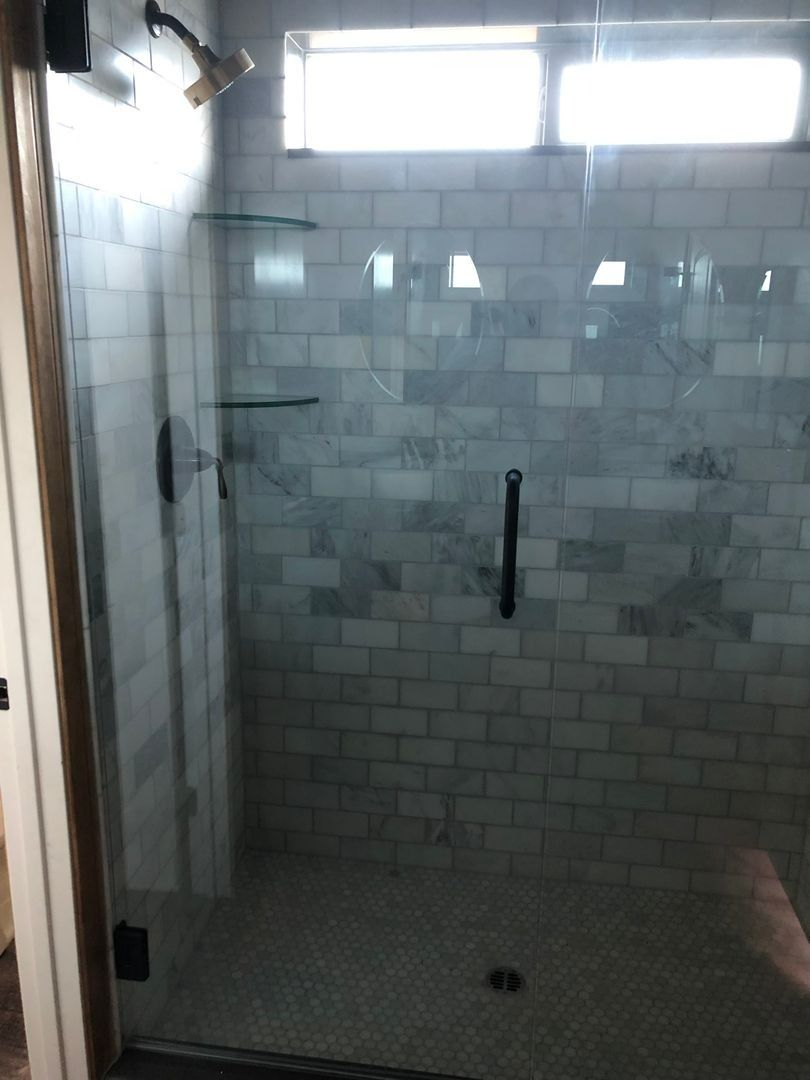 Empty tiled shower stall with bench, grab bar, and high windows.
