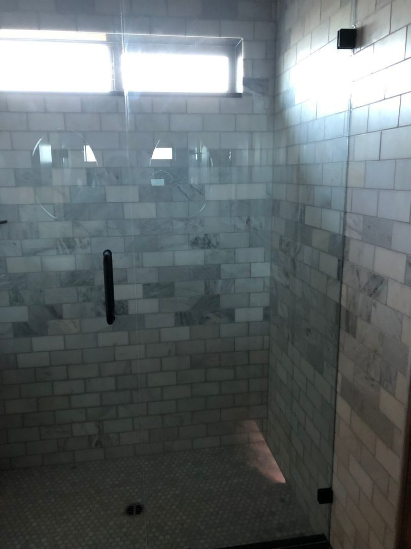 Empty tiled shower stall with a small window and black grab bar.
