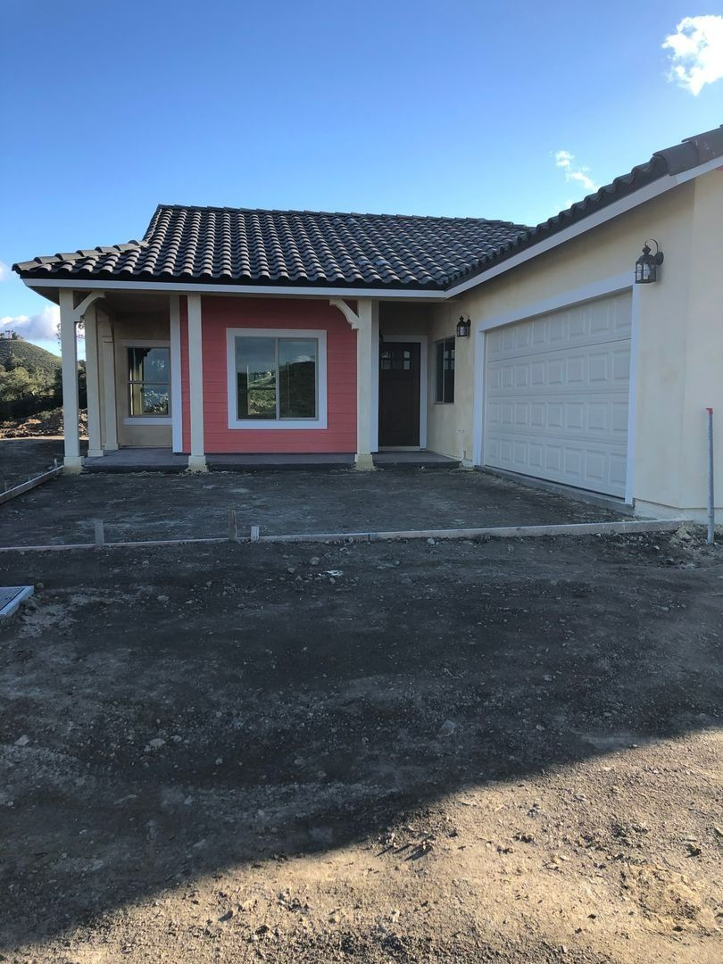 Single-story house exterior with pink front wall, white garage, and driveway under a blue sky