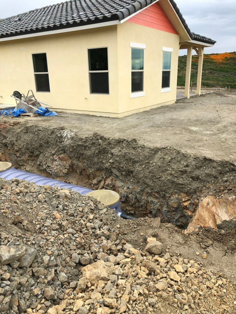New house exterior with unfinished dirt trench and gravel in the foreground