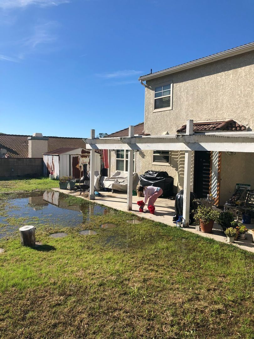 Backyard with a flooded lawn, patio, and a person bending near the house under a blue sky