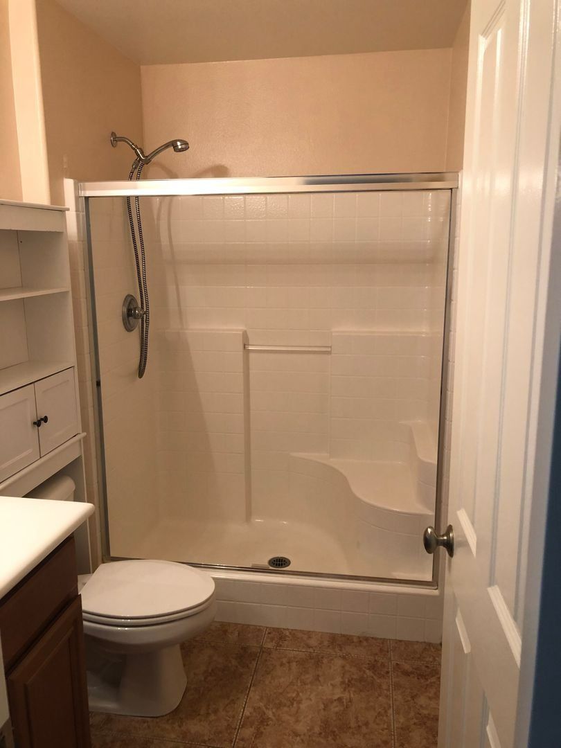 Small beige bathroom with a shower/tub combo, toilet, vanity, and open door.