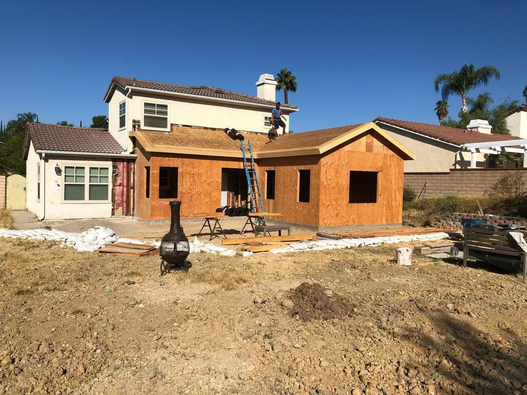 Partially built house with wood framing and stucco walls in a dirt yard under a clear blue sky